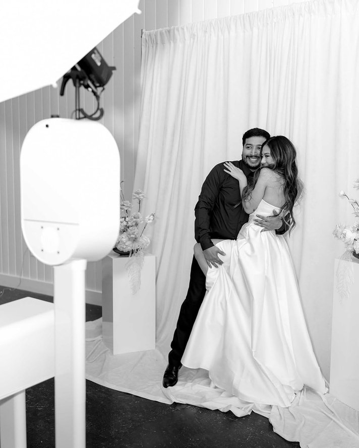 A couple embracing beside the white photo booth and its studio light.