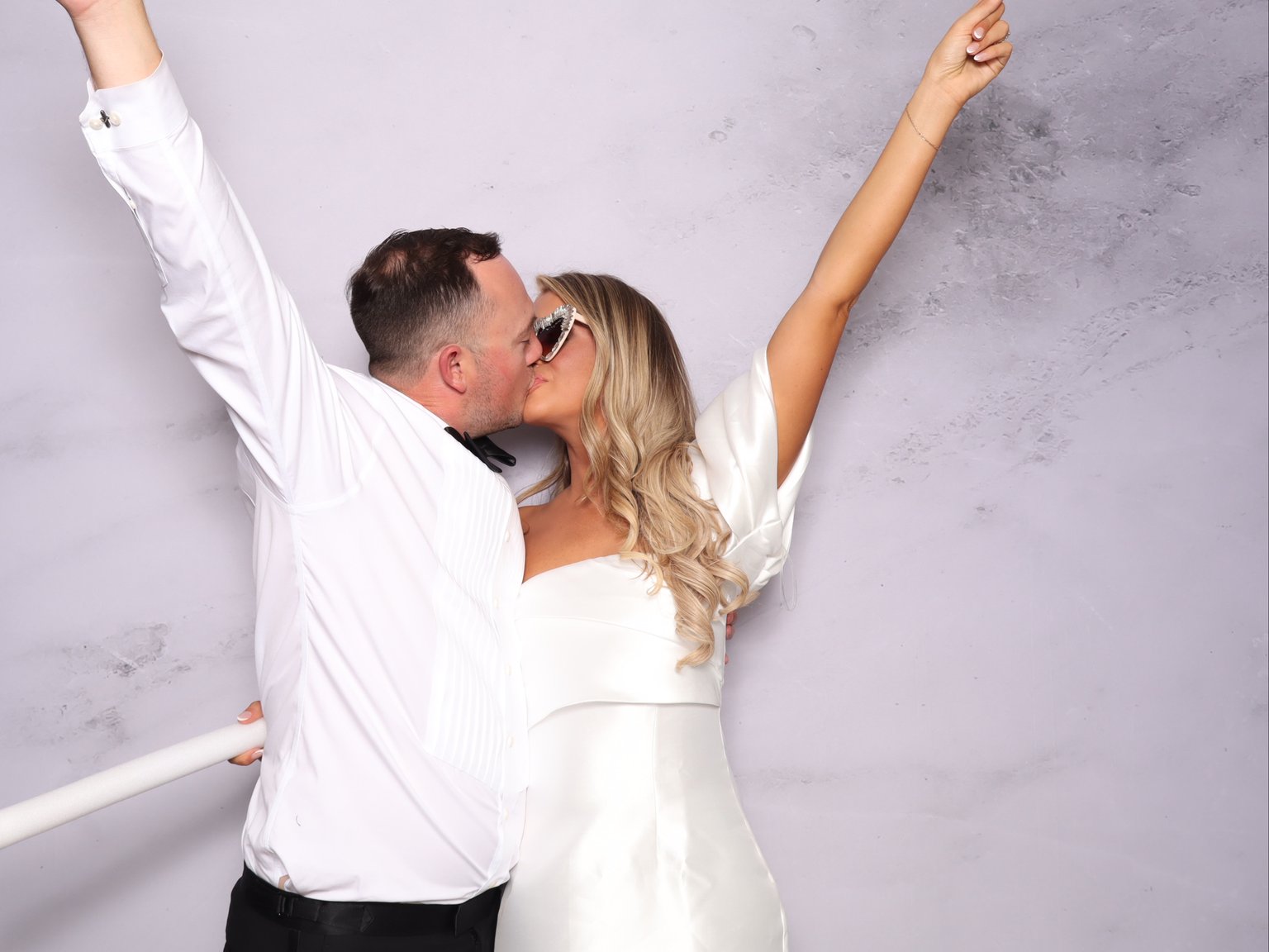 A bride and groom kissing, arms raised, at the photo booth.