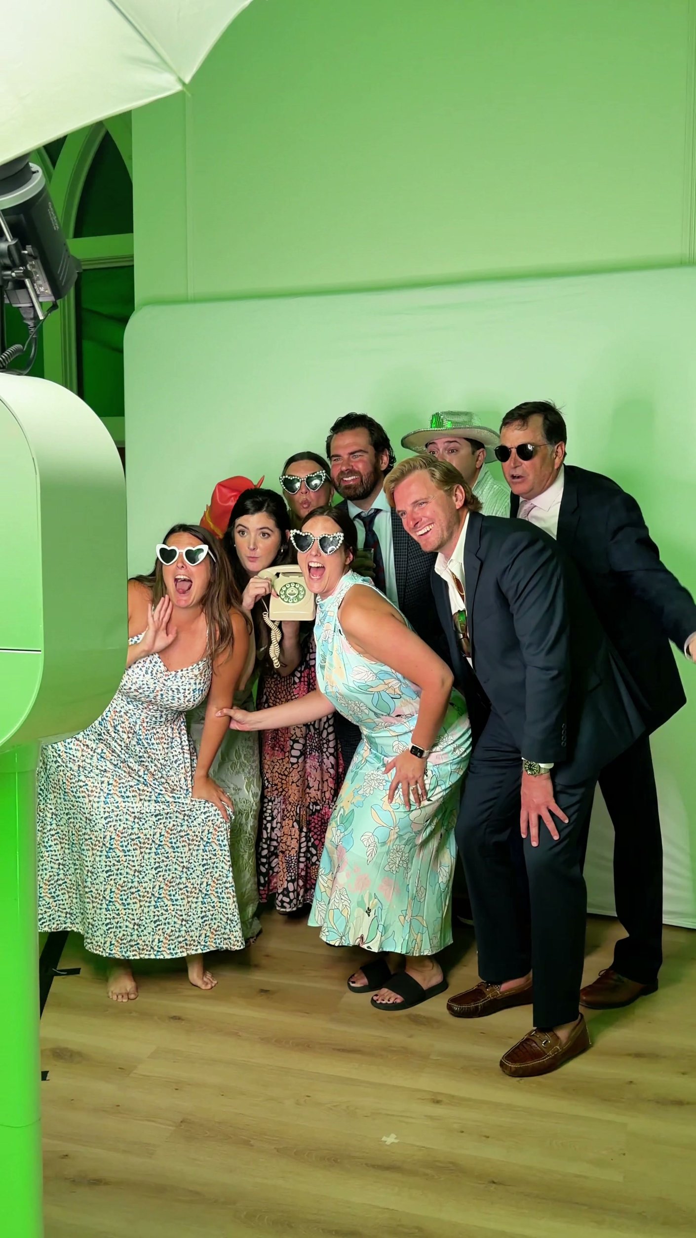 Guests in heart sunglasses posing at a green backdrop beside the photo booth.