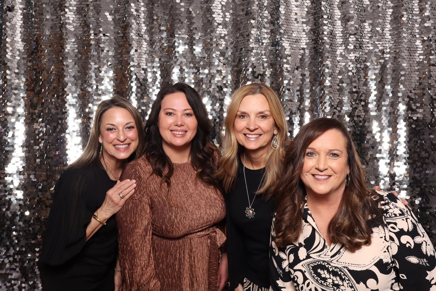 Four women posing in front of a silver sequin backdrop.